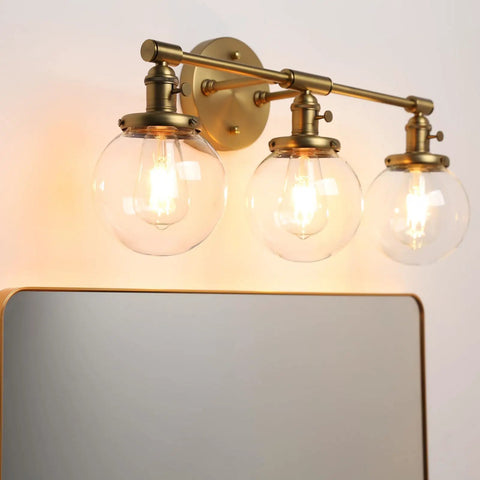 Three Light Vintage Industrial Bathroom Vanity Wall Sconce With Handblown Clear Glass Globes And Antique Gold Finish, 25.2 Inch Wide Triple Light Bath Fixture For A Soft Industrial Look over a mirror