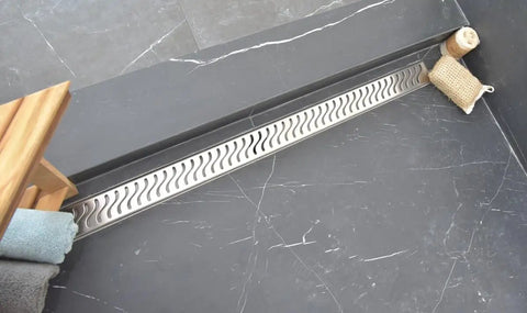 Twenty Three Half Inch Linear Shower Drain With Heavy Gauge Stainless Steel Frame And Ocean Wave Pattern in modern bathroom setting.