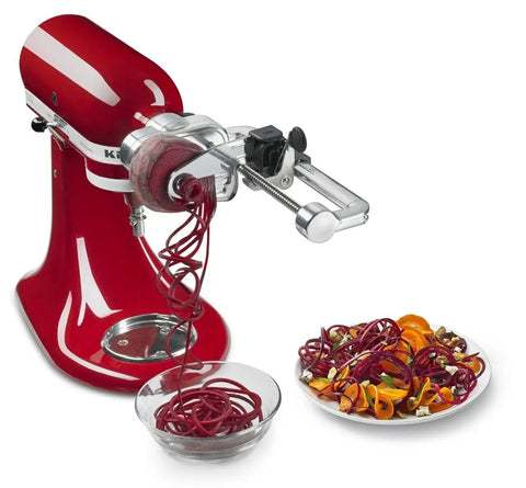 Red stand mixer with 7 Blade Spiralizer Plus With Peel Core And Slice Attachment slicing beet spirals into a glass bowl