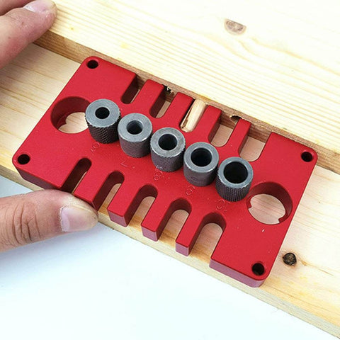 Red aluminum Punch Positioner Dowel Jig 3-In-1 Drill Guide Block for woodworking with metal guides on wooden board