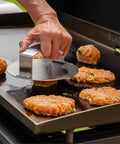 Hand using Smash Burger Press For Griddle And Grill Juicy Inside Crispy Outside Patties In Seconds Meat And Veggie Patty Maker on griddle.