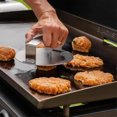 Hand using Smash Burger Press For Griddle And Grill Juicy Inside Crispy Outside Patties In Seconds Meat And Veggie Patty Maker on griddle.