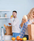 Woman packing groceries in kitchen with Bulk 500 Pack Heavy Duty Kraft Paper Bags 10x13 Inches With Handles, man in background.