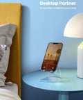 Clear Acrylic Cell Phone Stand For Your Desk And Office holding a smartphone on a blue nightstand with a lamp