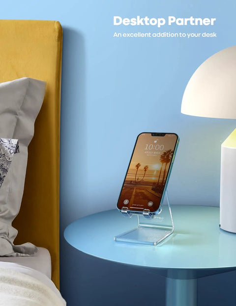 Clear Acrylic Cell Phone Stand For Your Desk And Office holding a smartphone on a blue nightstand with a lamp