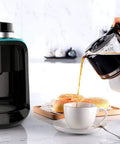 Hassle Free Mini Coffee Maker With Built In Bean Grinder And Glass Carafe pouring coffee into a cup with pastries nearby.