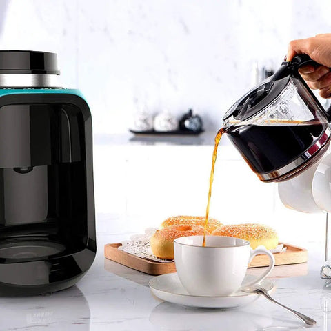 Hassle Free Mini Coffee Maker With Built In Bean Grinder And Glass Carafe pouring coffee into a cup with pastries nearby.