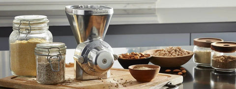 KitchenAid KGM all-metal grain mill attachment, front view on kitchen counter with jars of grains.