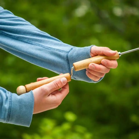 Person holding Marshmallow Roasting Sticks Set Of 2 With Multiple Attachments for campfire cooking, showing easy spin handle.