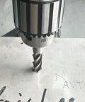 HSS 4-flute straight end mill cutter in a drill chuck cutting into a metal plate.