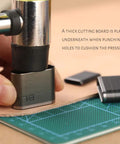 Close-up of using a 52 Shape Style Leather Hole Punch Tool Set With 52 Shapes on a leather strip, featuring a hammer and cutting mat.