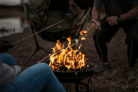 People roasting marshmallows over a 22 Inch Outdoor Wood Burning Fire Pit With Mesh Lid And Fire Picker Durable Alloy Steel Pit.