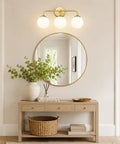 Dope Mid Century 3 Light Vanity Fixture With Smooth Brushed Gold Finish And Soft Milky White Glass Ball Shades above a mirror.