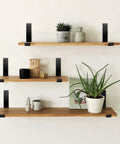 Matte Black J Lip Wall Shelf Brackets Hella Sturdy 8 Pack supporting wooden shelves with plants and decor on a wall.