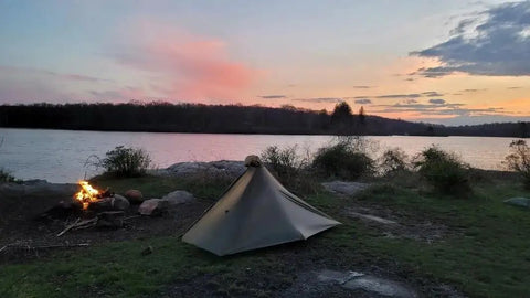 Gatewood Cape Ultralight 11 Oz Backpacking Tarp Shelter And Poncho Canopy, pitched by a lakeside at sunset, green.