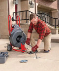 Technician using Heavy Workhorse 115 Volt Drain Cleaning Machine With Auto Feed Cable Control and 5 8 Inch Tool Kit for sewer line.