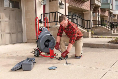 Technician using Heavy Workhorse 115 Volt Drain Cleaning Machine With Auto Feed Cable Control and 5 8 Inch Tool Kit for sewer line.