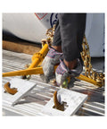 Person using Heavy Duty Ratchet Load Binder For 3/8 To 1/2 Inch Grade 70 Transport Chain, yellow finish, on flatbed trailer.