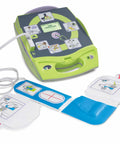 Front view of a green AED Plus trainer with CPR-D pads, blue training pads, and a carry case.