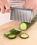 Stainless steel crinkle cutter with wavy blade slicing cucumber on cutting board