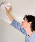 Woman installing the Rock Solid Hardwired Smoke Detector With Whole Home Interconnect Readiness And Dependable Backup Power For Straight Talk Fire Safety Plus Nailed Down Installation And Snappy Hush Response.