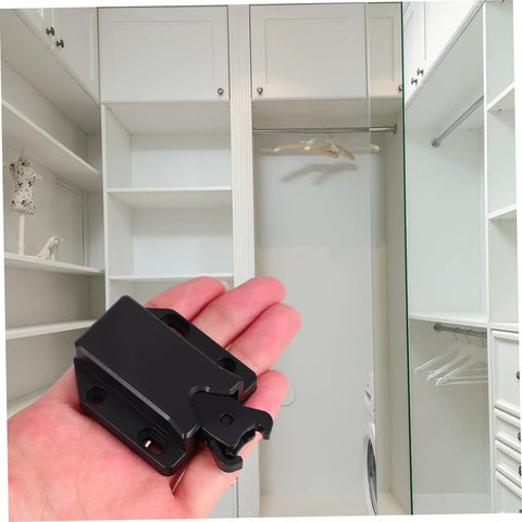 Holding a black Push To Open Cabinet Latch Kit Four Pack With Rebound Tech for cabinets and closets in front of a white closet.
