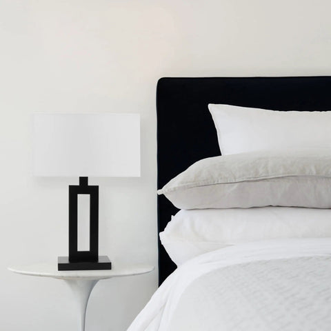 D'Alessio Table Lamp In Matte Black With Modern Cutout Body And White Linen Shade, 20 Inch Tall, on white bedside table