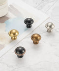 Five different finishes of cabinet knobs laid on a marble surface, including Ten Pack One And One Quarter Inch Antique Brass Kitchen Cabinet Knobs.