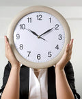 Person holding large round clock face up covering their face