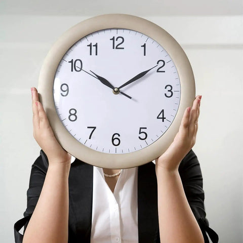 Person holding large round clock face up covering their face