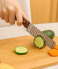 Crinkle cutter knife with wooden handle, 5-inch stainless steel wavy blade, slicing cucumber on cutting board.