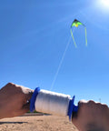 Flying kite with Kite Spool Reel Winder With Grip String Handles, 600 Feet Twisted Polyester Line, held by hands on a sunny day.