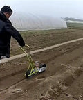 Person using the Hand Push Garden Seeder With Metal Precision Hopper Walk Behind Row Crop Planter Manual Roller Seeding For Even Spacing And Depth Includes Seed Storage Box Durable Backyard Agriculture Tool For Sowing Seeds on farmland.