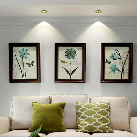 Top Shelf 14 Pack Recessed Led Ceiling Lights With Three Color Dimming And Slick Copper Trim For Modern Living Rooms Energy Saving Ambient Glow Quick Install Solid Home Fixtures illuminating framed botanical art above a light sofa.
