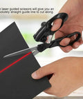 Laser-guided sewing scissors with ergonomic black handles and red laser guide cutting black paper.