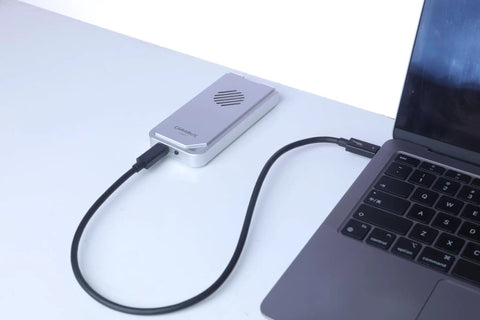 USB4 NVMe Enclosure With Active Cooling Fan And Solid Aluminum M.2 SSD Case connected to laptop via USB cable.