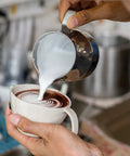 Pouring milk from 12oz Stainless Steel Milk Frothing Pitcher For Latte Art Pro Grade Barista Steam Pitcher With Inner Measurements Easy Pour Milk Jug And Decorating Pen Rustproof Dishwasher Safe Perfect For Cappuccino And Latte into a cup with latte art.