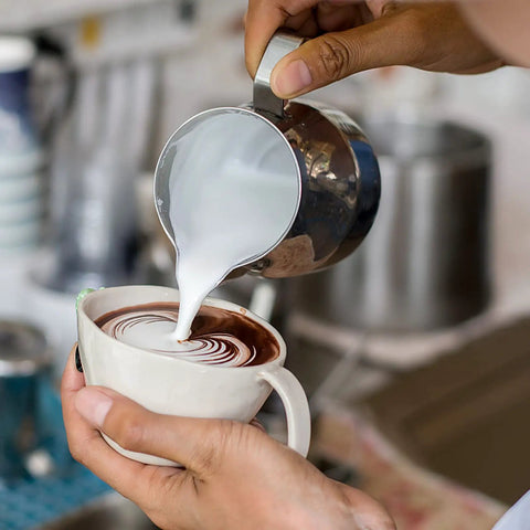 Pouring milk from 12oz Stainless Steel Milk Frothing Pitcher For Latte Art Pro Grade Barista Steam Pitcher With Inner Measurements Easy Pour Milk Jug And Decorating Pen Rustproof Dishwasher Safe Perfect For Cappuccino And Latte into a cup with latte art.