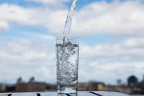 Glass of water being poured from an electric portable water dispenser pump on an outdoor table with a blurred skyline background.