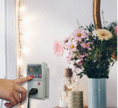 Person using Kill A Watt EZ Electricity Usage Monitor for Home Energy Savings and Real Time Cost Forecasts, mounted on wall.