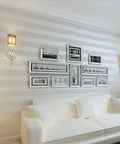 European Modern Minimalist Country Stripe Wallpaper Roll For Living Room Bedroom And TV Backdrop In Cream White Non Woven Eco Friendly Material With Rich Texture Subtle Gloss And Enhanced Depth For A Cozy Home Vibe on living room wall with framed pictures above white sofa.