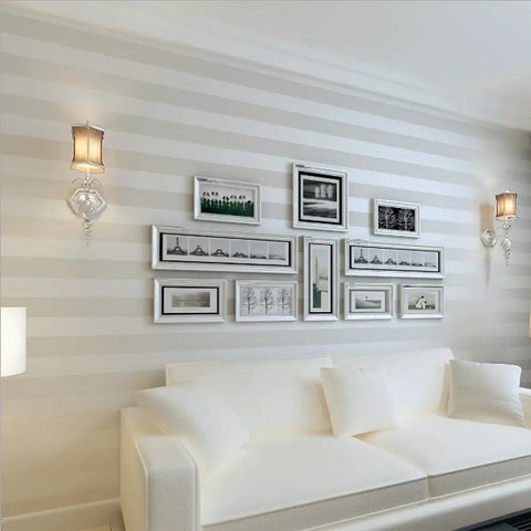 European Modern Minimalist Country Stripe Wallpaper Roll For Living Room Bedroom And TV Backdrop In Cream White Non Woven Eco Friendly Material With Rich Texture Subtle Gloss And Enhanced Depth For A Cozy Home Vibe on living room wall with framed pictures above white sofa.
