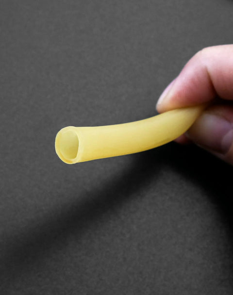 Yellow latex rubber tubing held between fingers; flexible medical/lab tubing.