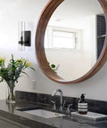 Modern Farmhouse Glass Cylinder Wall Sconce 1 Light Black Vanity Light Fixture mounted in a bathroom with round mirror and flowers.