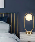 Gold Brass Finish Oval Bedside Table Lamp With Milky White Shade next to a bed, creating a cozy glow in the bedroom.