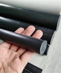 Close-up of PTFE Solid Bar With Graphite Filler For Smooth Sliding 10 To 50 Mm Diameter 50 Cm Length in hand showing black color