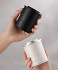 Two hands holding a black and a white Total Game Changer Aluminum Coffee Dosing Cup And Espresso Digital Scale Combo.