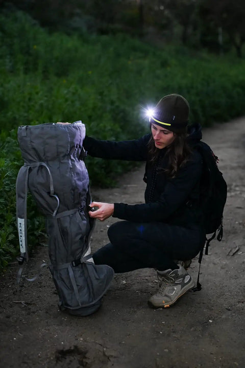 Hiker wearing Ultra Bright 5 Mode LED Headlamp for Adults with USB Rechargeable Battery, adjusting backpack on a night trail