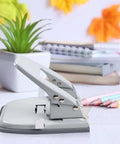 2 Hole Punch for Paper with adjustable guides on a desk, with a locking handle and metal design, next to office supplies
