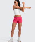 Woman stretching in Low Waisted Running Shorts 2.5 Inch Inseam In Lip Gloss Pink With Built-In Mesh Liner, Friction-Reducing, Side Zip Pocket